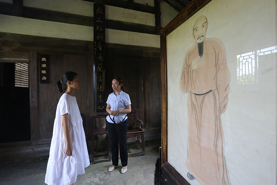 在故居前正屋内，面对魏源肖像，焦佳（右一）给胡亦珂弘讲解纶音箱的来历。图片来源：湖南文明网 记者 彭团 实习生 孙豆豆 摄