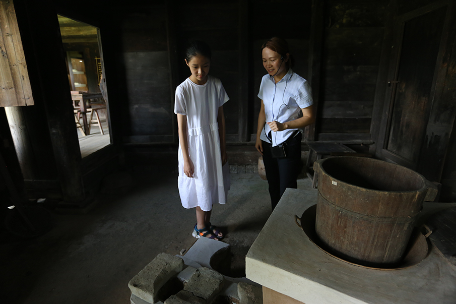 在灶屋，焦佳（右一）给胡亦珂弘指出灶台，并说这个灶台就是现在农村比较普遍使用的灶。图片来源：湖南文明网 记者 彭团 实习生 孙豆豆 摄